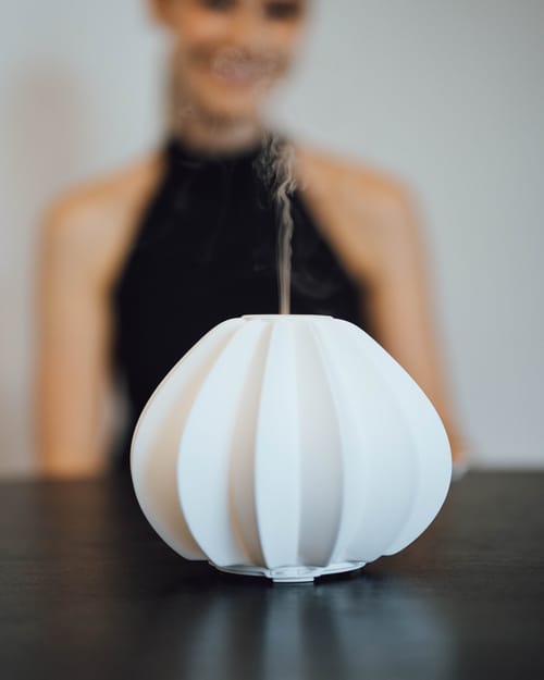Aromadiffuser auf einem dunklen Tisch, im Hintergrund unscharf eine Frau