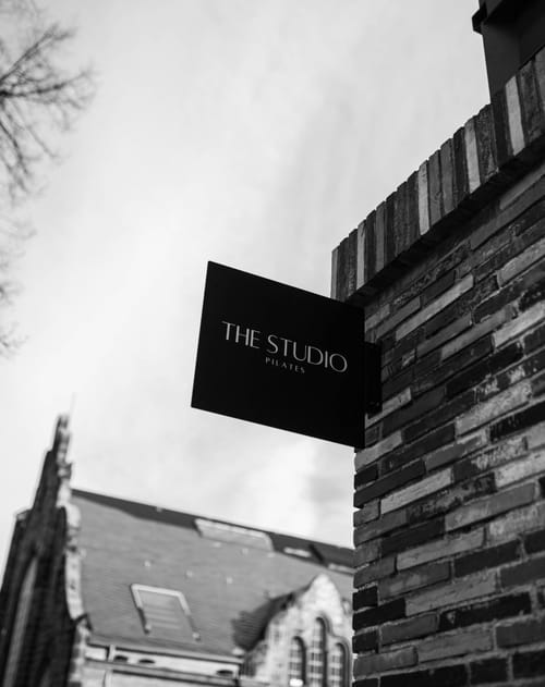 Schwarz-Weiß-Aufnahme des Schilds „The Studio Pilates“ an einer Backsteinfassade