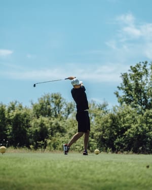 Tim Stützle nach dem Golfschwung vor Bäumen und blauem Himmel