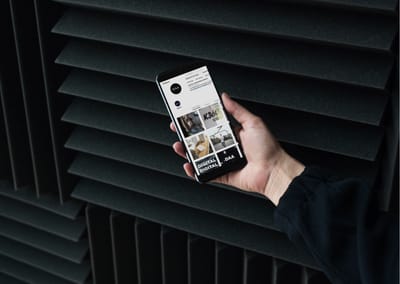 Hand hält ein Smartphone mit dem Instagram-Profil der DAA vor dunklen Lamellen