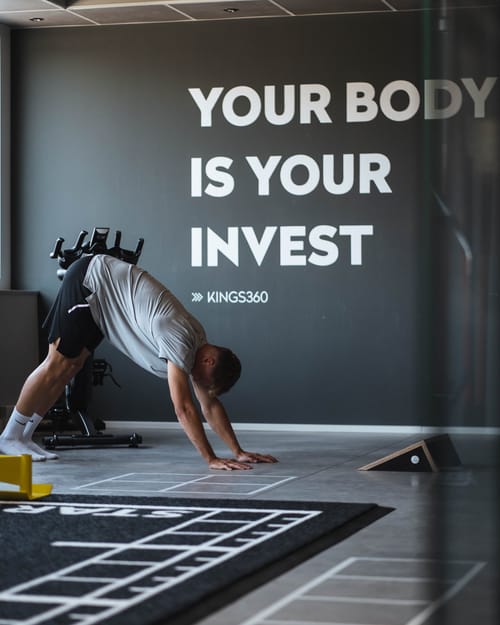 Dehnübung im Trainingszentrum, an der Wand der Schriftzug „Your Body is your Invest“