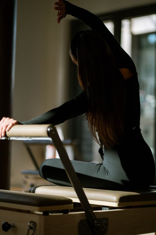 Frau in schwarzer Trainingskleidung dehnt sich auf einem Reformer, von hinten fotografiert