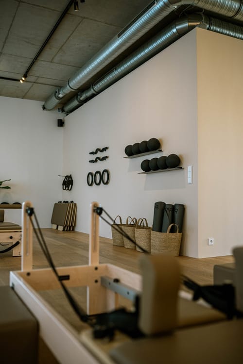 Wand mit Pilates-Equipment – Bälle, Ringe und Matten –, im Vordergrund ein Reformer
