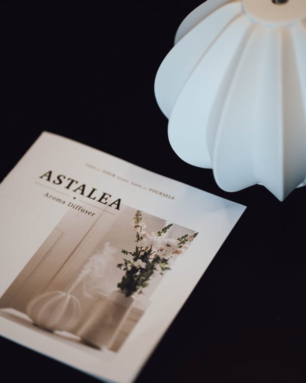 ASTALEA-Aromadiffuser neben einer aufgeschlagenen Broschüre auf dunklem Untergrund