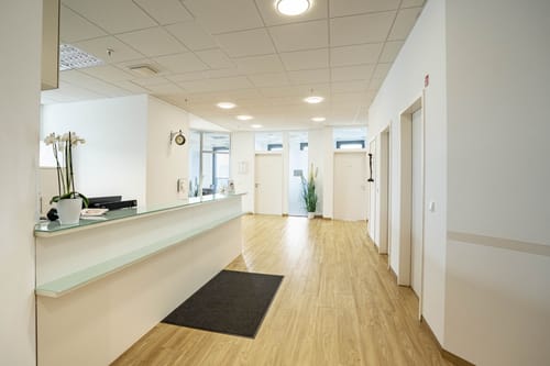 Heller Empfangstresen mit Glasablage und Orchidee, dahinter Flur mit Holzboden